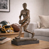 AFL football player bronze sculpture mid-run with oval ball, hyper-realistic Australian Rules Football statue on black marble base, loss wax casting sports art for trophies.