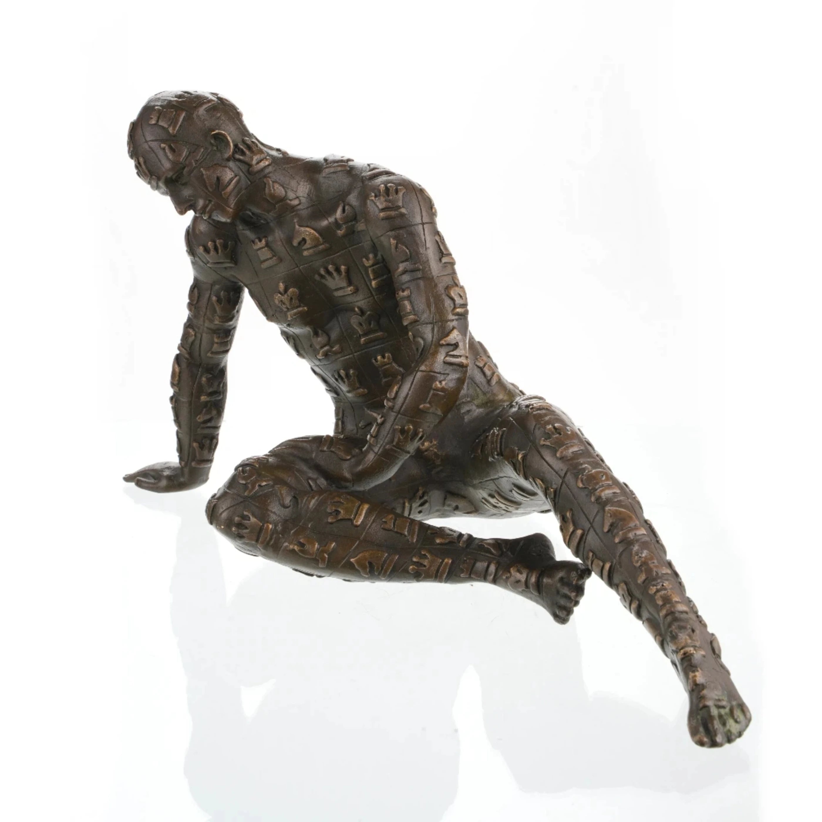 Contemporary bronze sculpture crouching male figure with chessboard symbols pattern, conceptual human form statue mid-movement, loss wax casting avant-garde art.