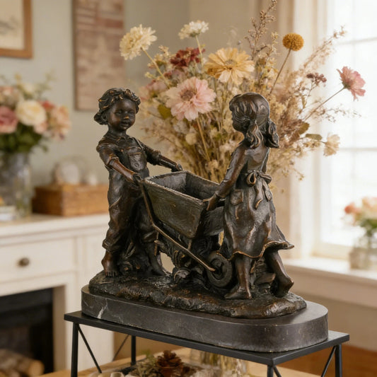 Nostalgic bronze sculpture of a boy and girl with a wheelbarrow on black marble base, heartwarming children playing art for home decor.
