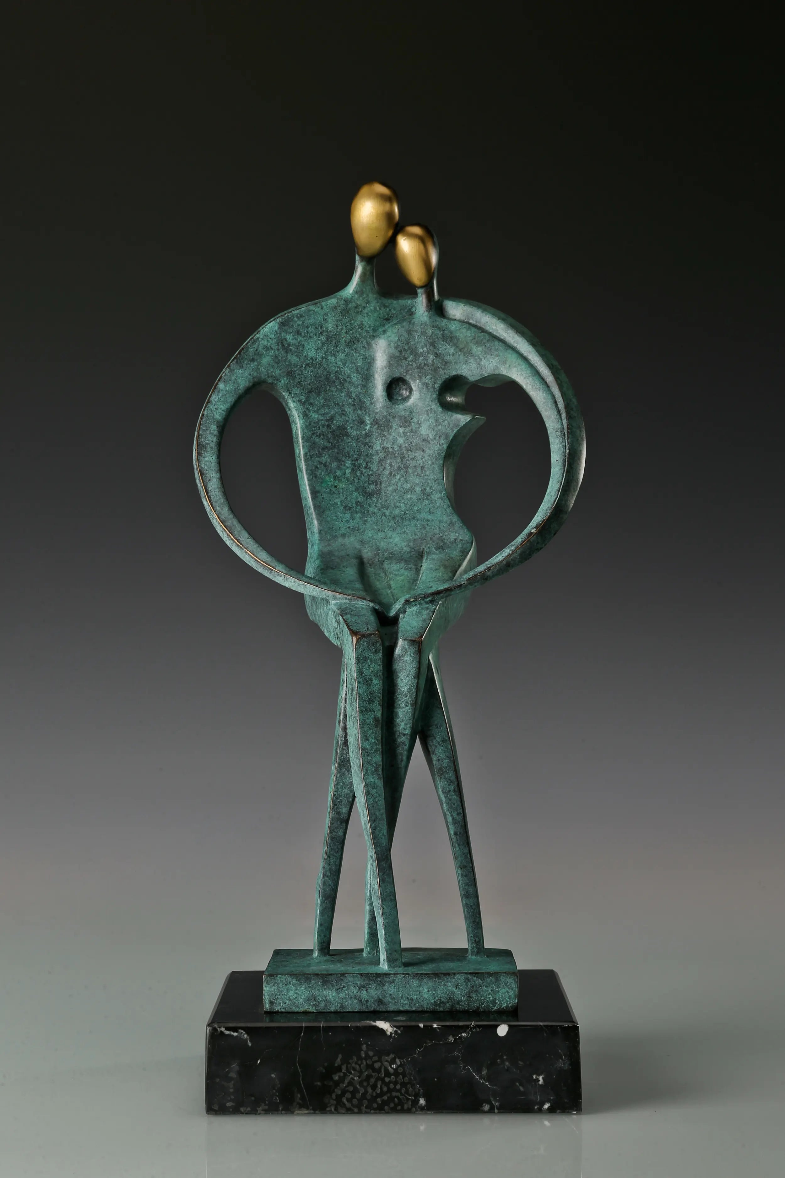 Front view of abstract couple bronze sculpture with two golden faces and heart-shaped arms