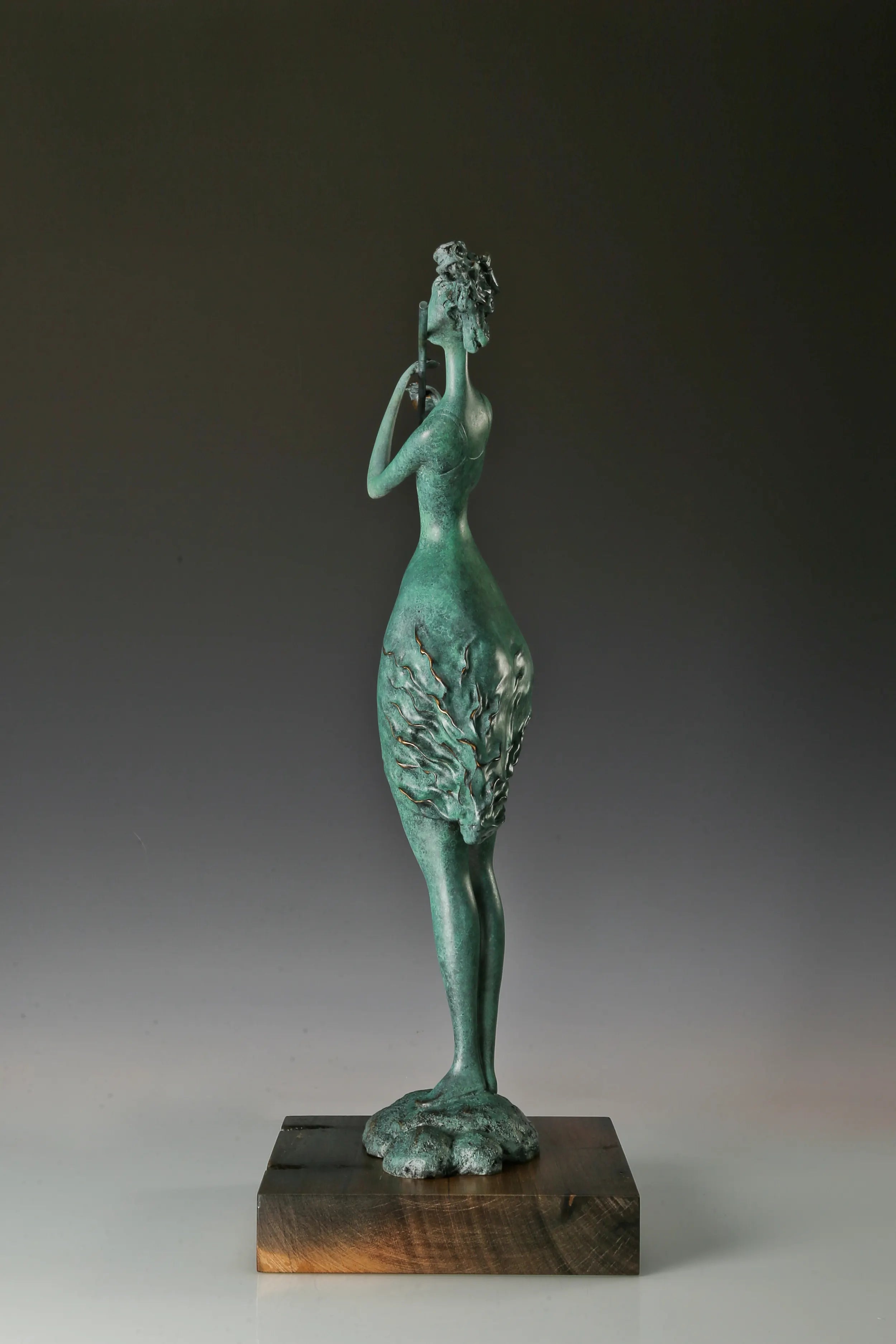 Side profile of abstract bronze woman playing a flute on a wooden base