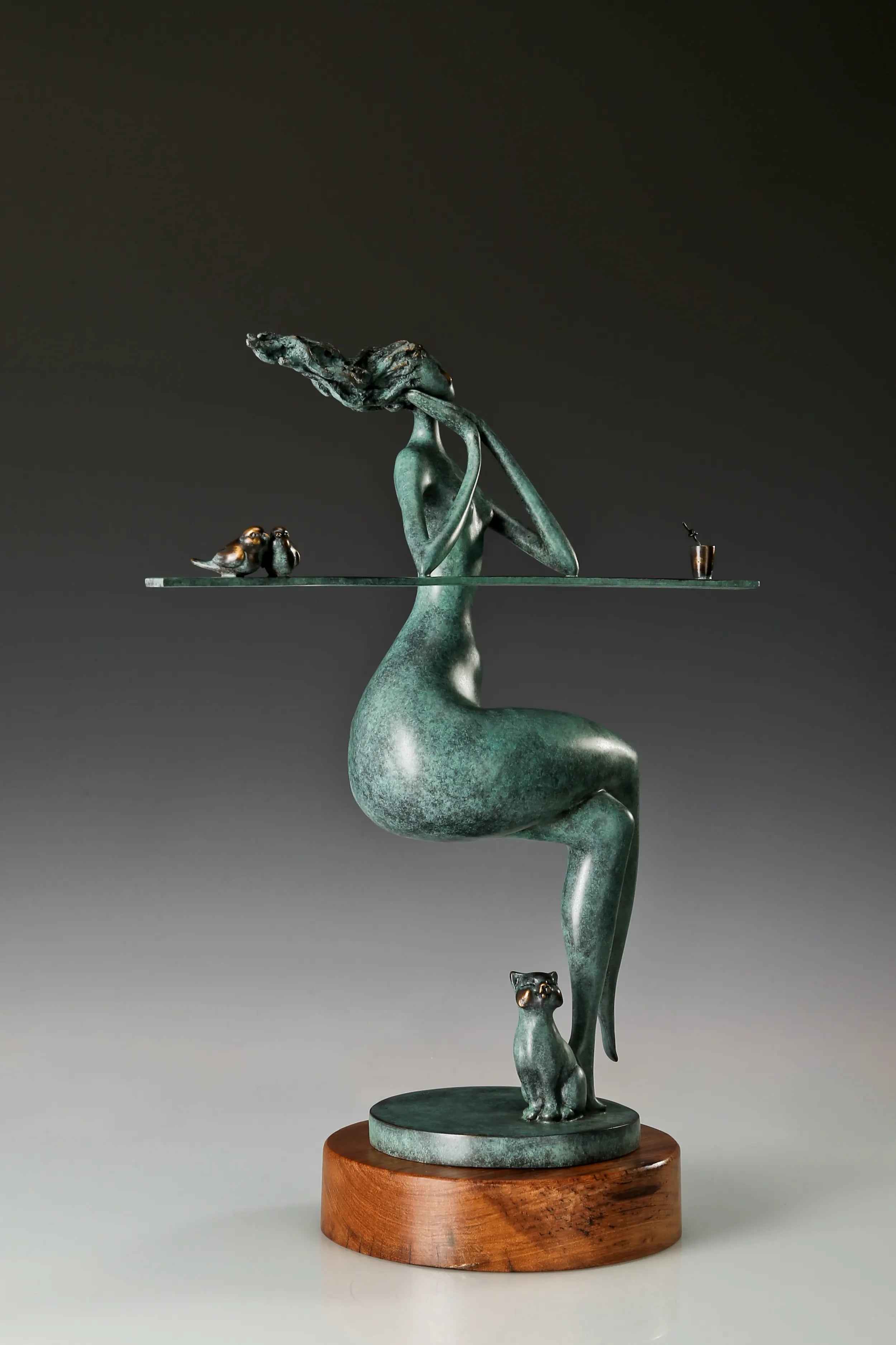 Three-quarter view of an abstract woman bronze sculpture featuring birds, a cat and a drink