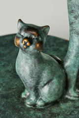 Close-up of a small bronze cat with golden facial accents sitting at the woman's feet