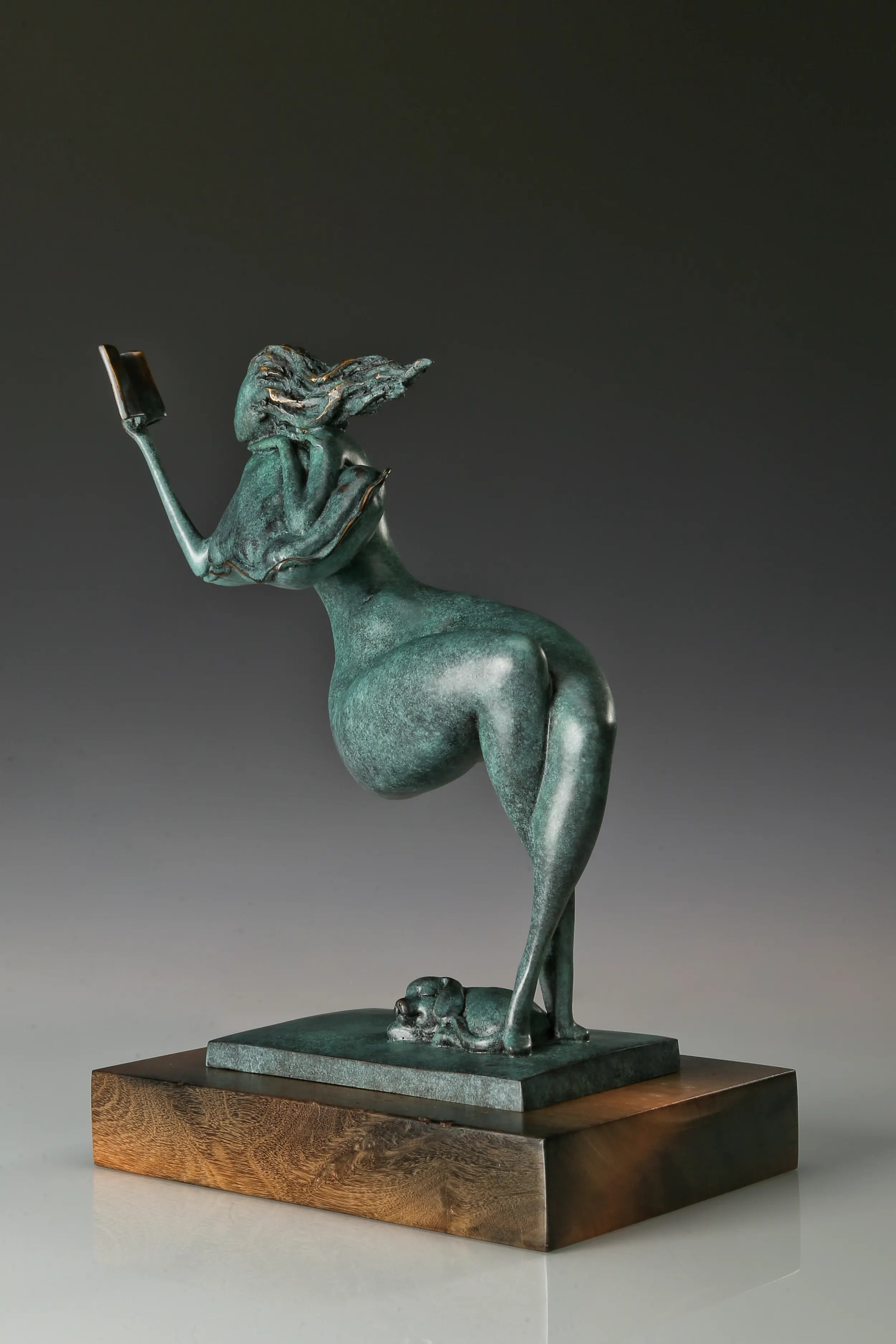 Angled view of an abstract woman reading a book with flowing hair and a green patina finish