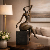Contemporary abstract bronze seated female sculpture with golden floral motifs, graceful woman statue with raised arm on black marble base, loss wax casting modern art.