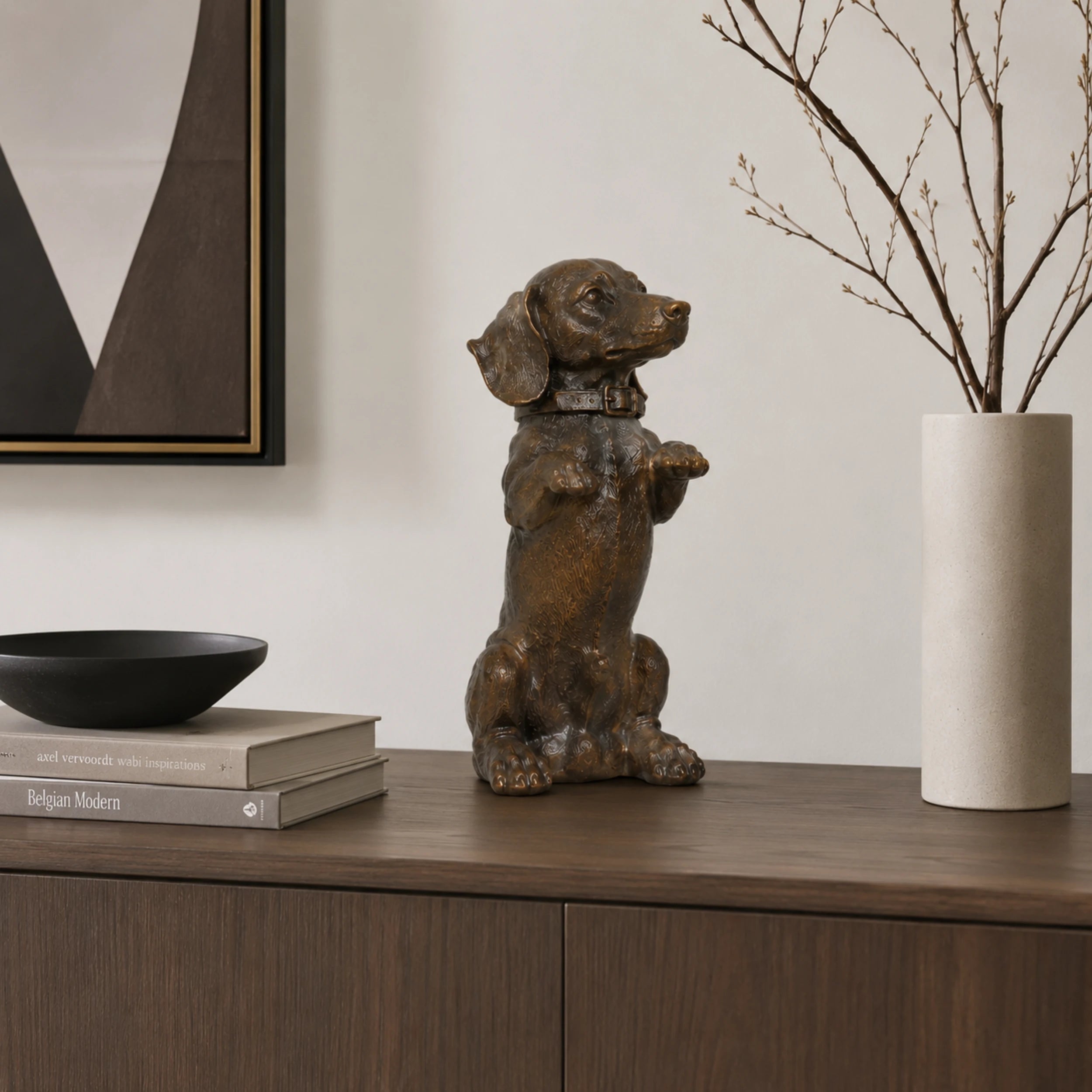 A charming bronze dachshund statue in a playful upright seated pose with front paws raised begging, highlighting its long body and short legs.