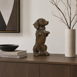 A charming bronze dachshund statue in a playful upright seated pose with front paws raised begging, highlighting its long body and short legs.