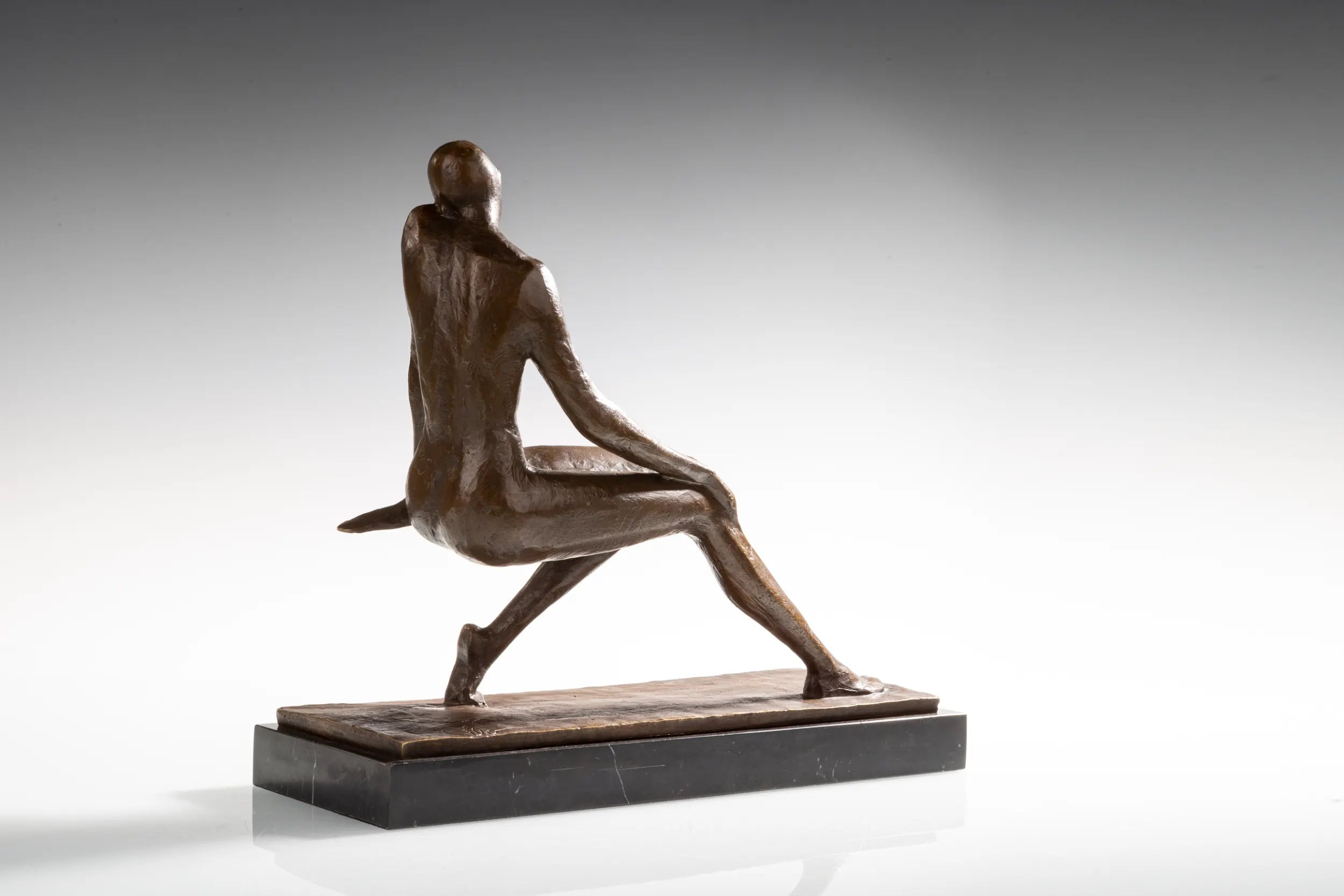 Rear angled view of bronze female figure with crossed legs and one arm resting behind her