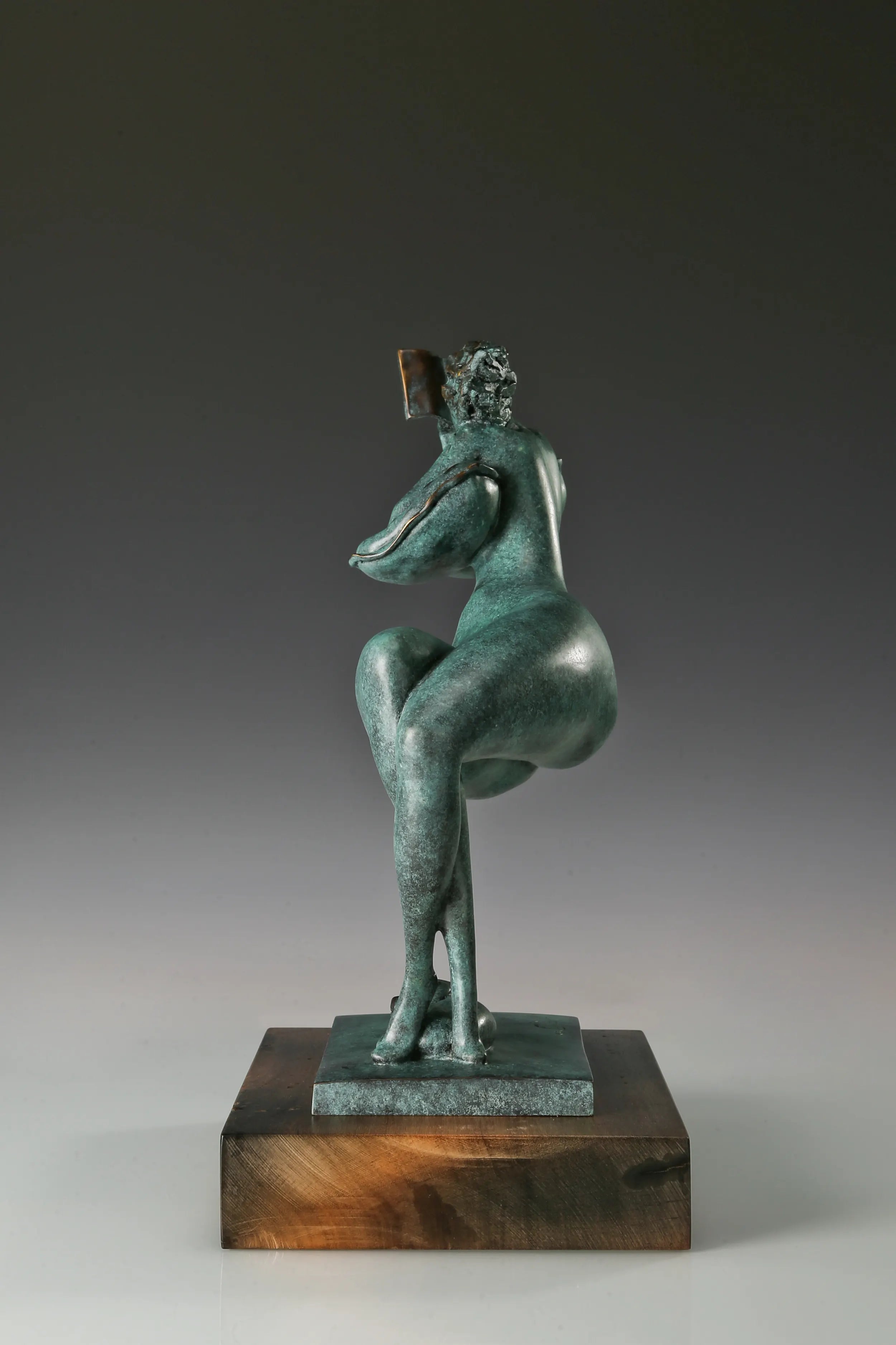 Right side view of a green patina bronze reading woman sculpture on a rectangular wooden base