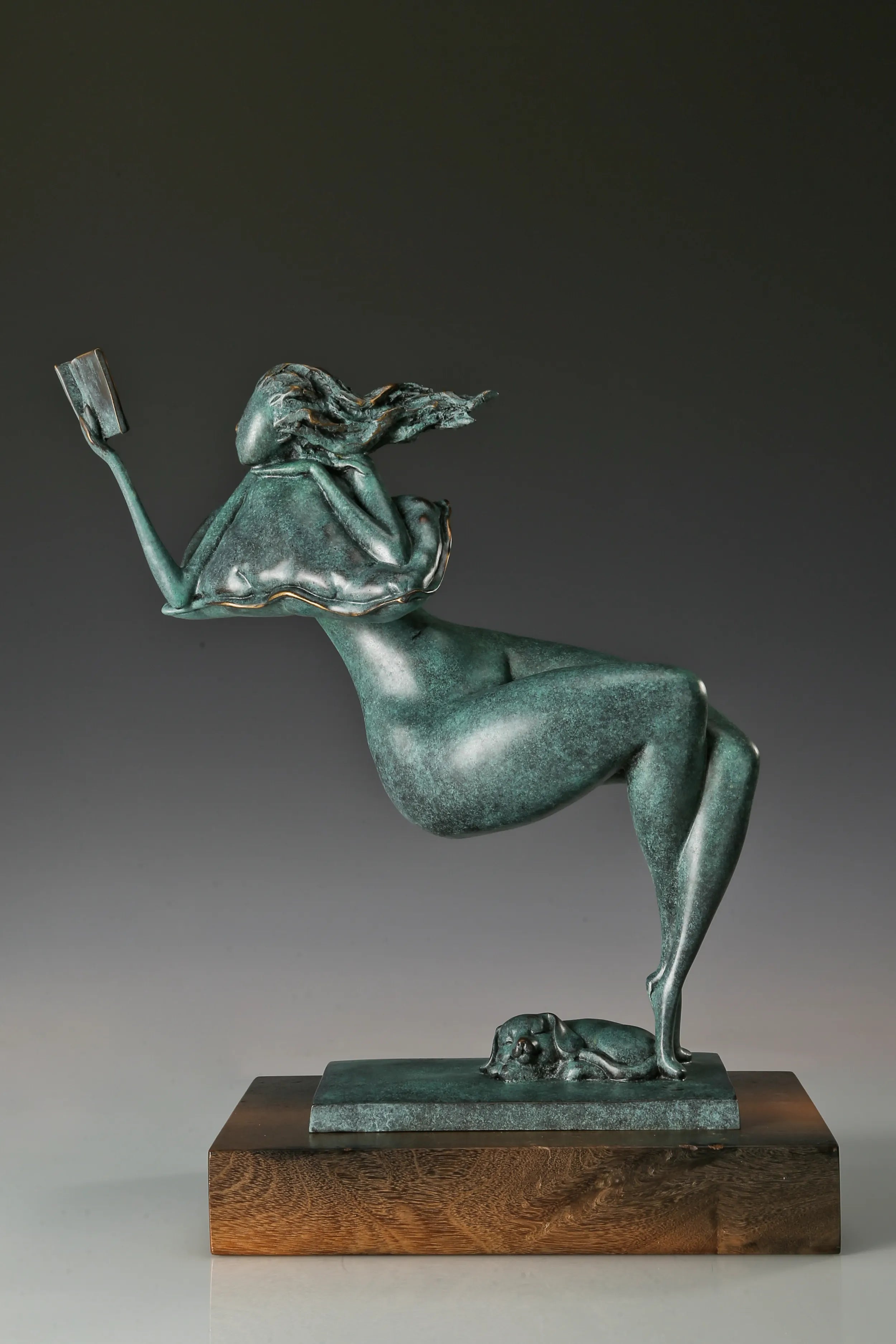 Side view of a reclining bronze woman holding a book with a small dog resting beneath her feet