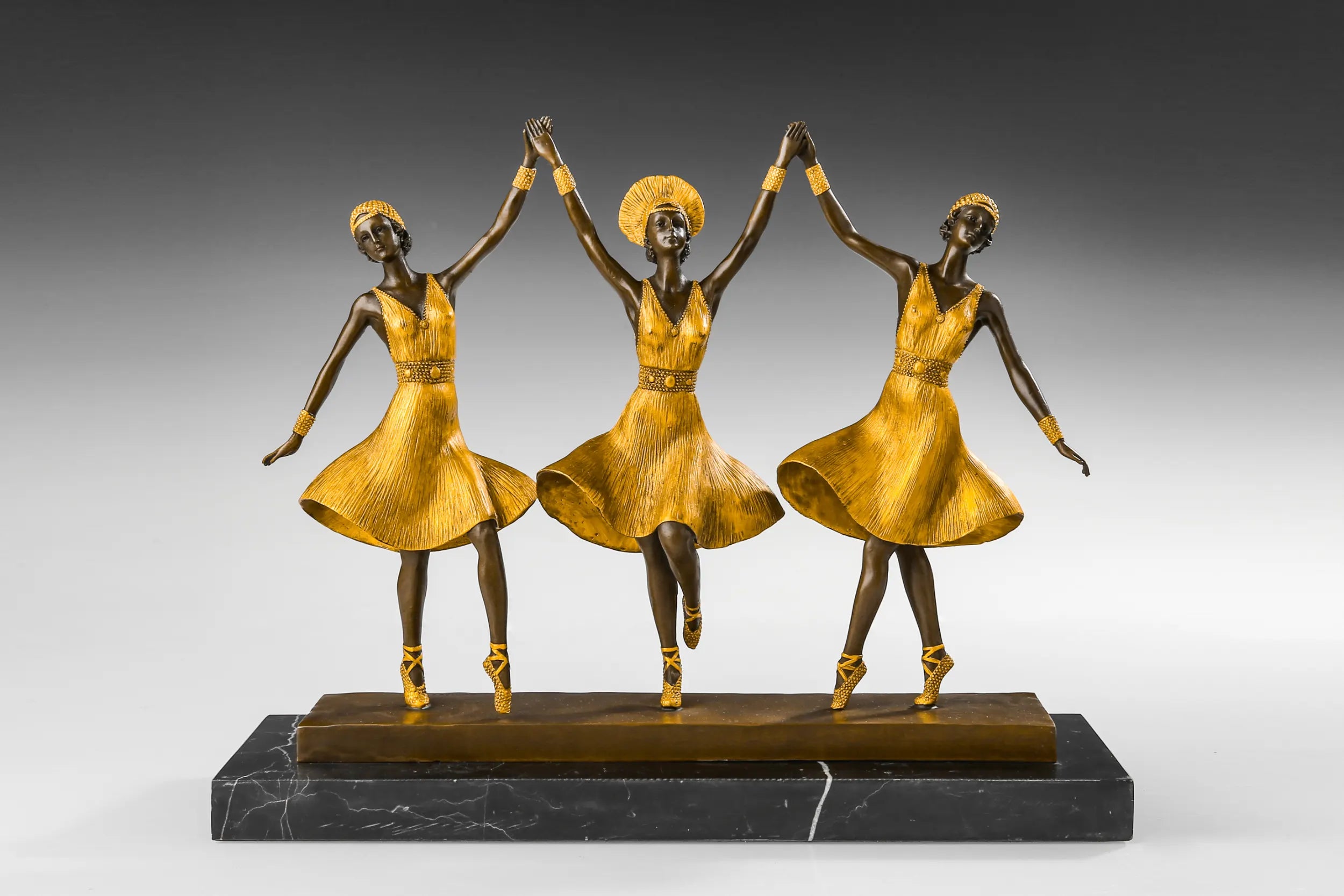 Front view of three ballerinas bronze sculpture with joined hands and golden dresses