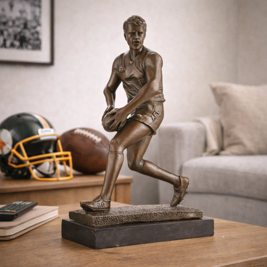 AFL football player bronze sculpture mid-run with oval ball, hyper-realistic Australian Rules Football statue on black marble base, loss wax casting sports art for trophies.