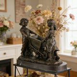 Nostalgic bronze sculpture of a boy and girl with a wheelbarrow on black marble base, heartwarming children playing art for home decor.