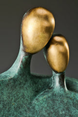 Close-up of two golden bronze faces leaning together on an abstract couple sculpture