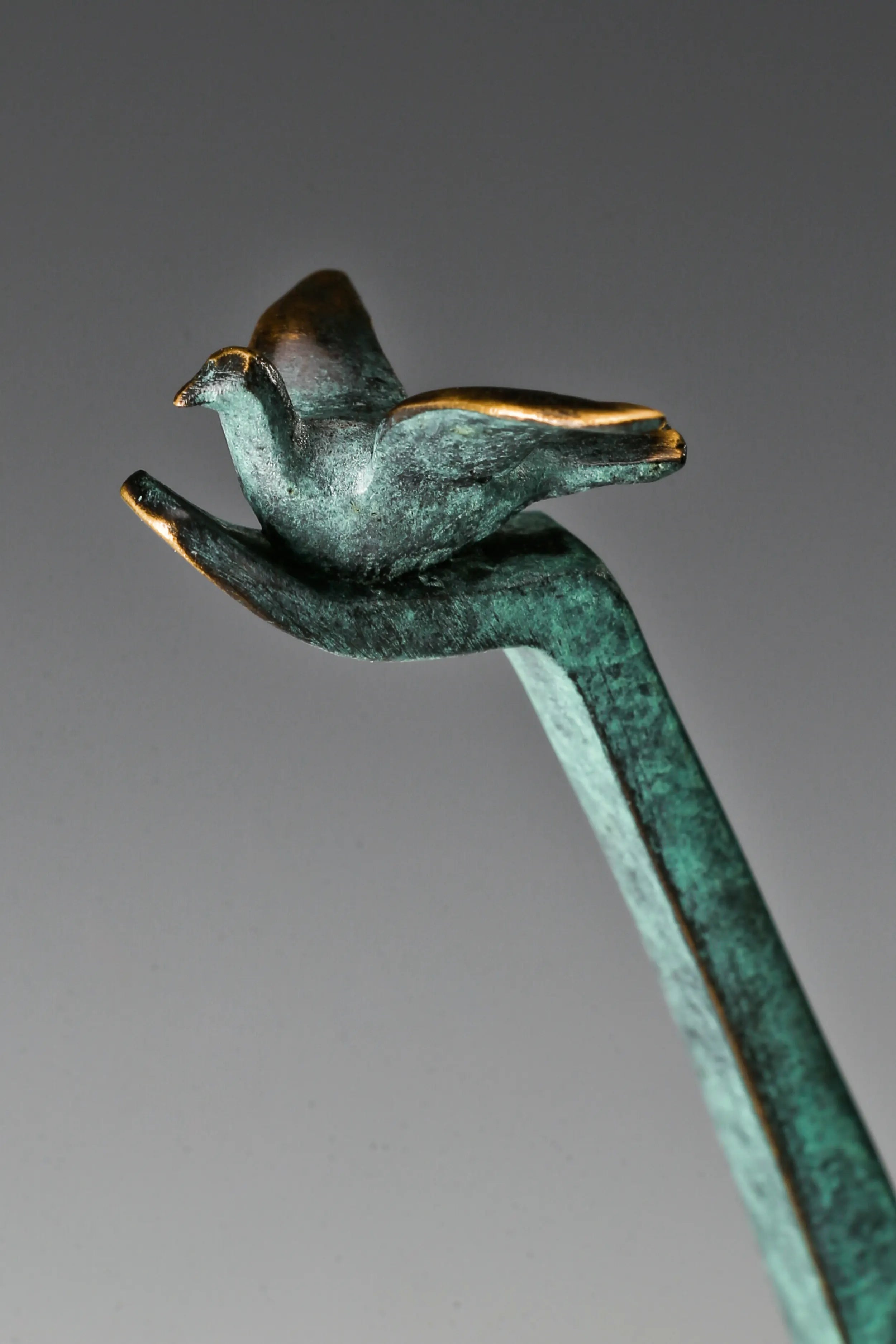 Close-up of a small bronze bird perched on the raised hand of an abstract figure