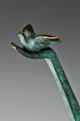 Close-up of a small bronze bird perched on the raised hand of an abstract figure