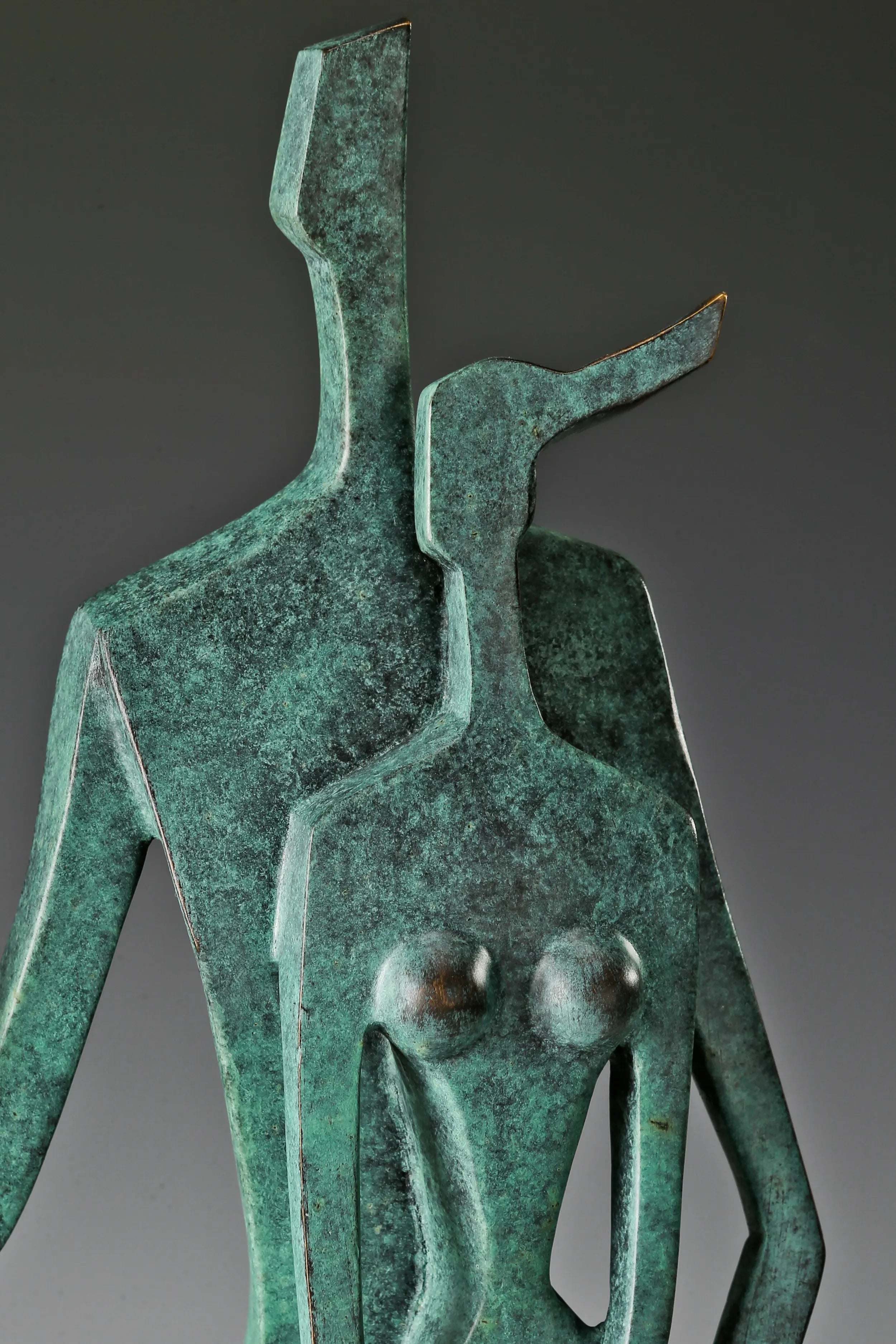 Close-up of two abstract bronze figures with geometric heads and textured green patina