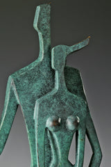 Close-up of two abstract bronze figures with geometric heads and textured green patina