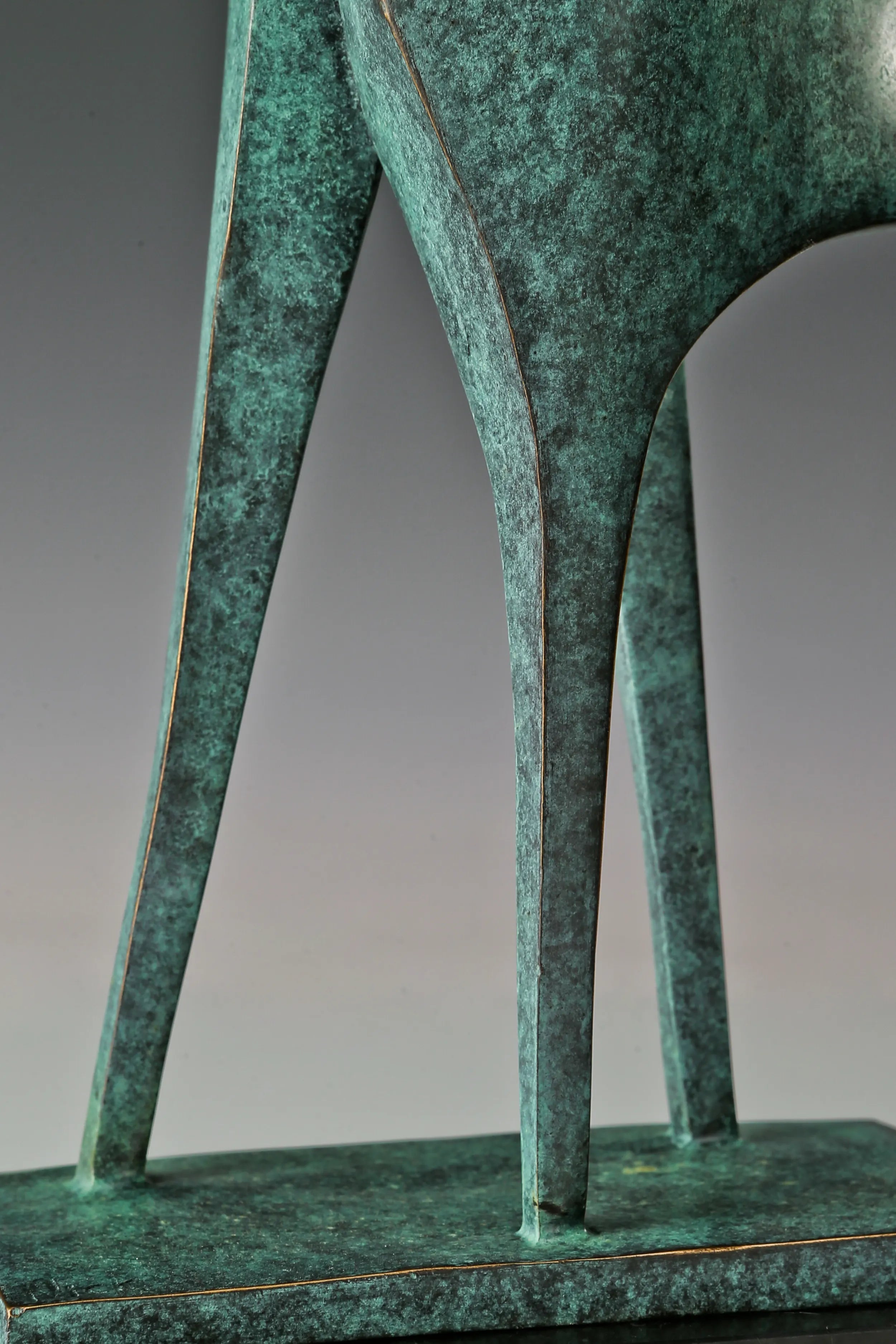 Detail of elongated bronze legs and angular lower forms with a green patina finish