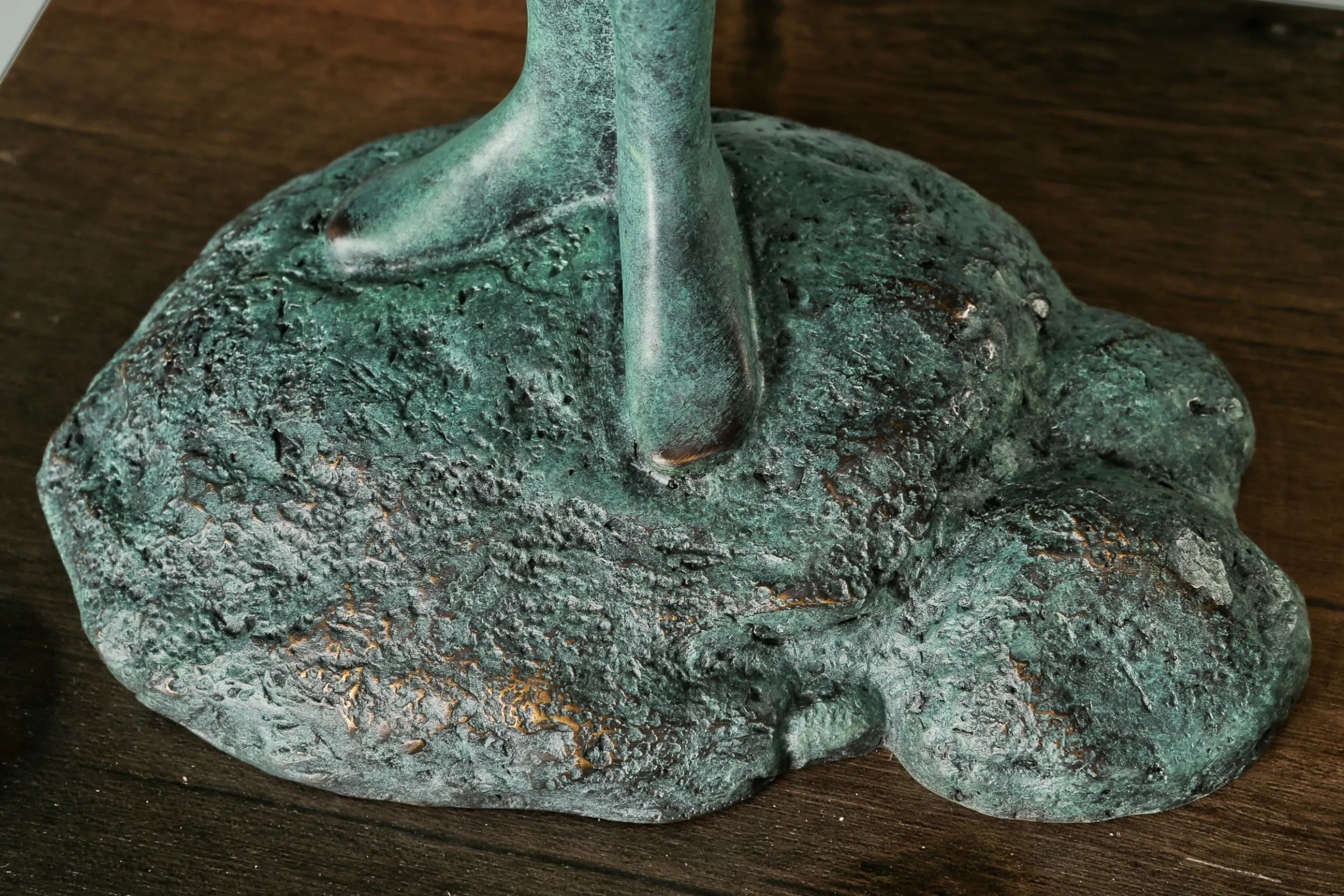 Close-up of the bronze figure's feet standing on a textured support above a wooden base