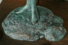 Close-up of the bronze figure's feet standing on a textured support above a wooden base
