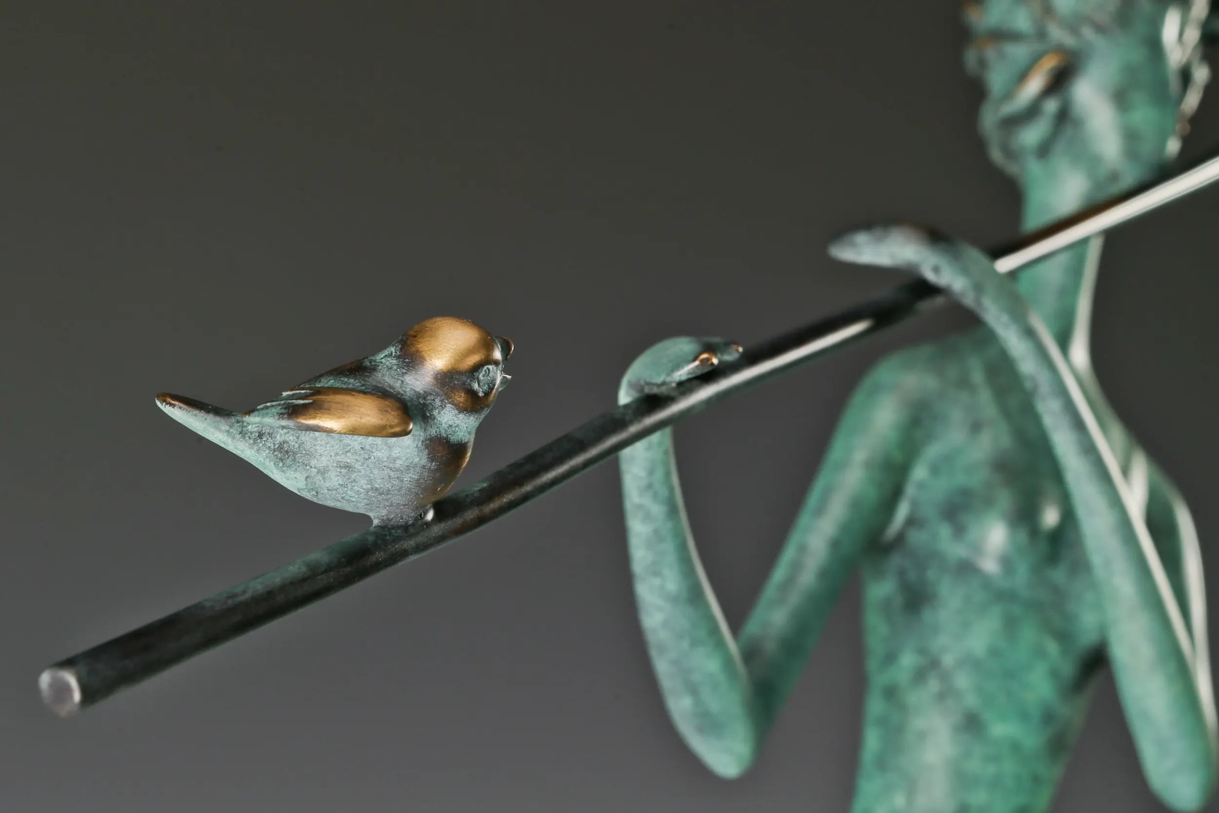 Close-up of a small bronze bird with golden accents perched on the flute