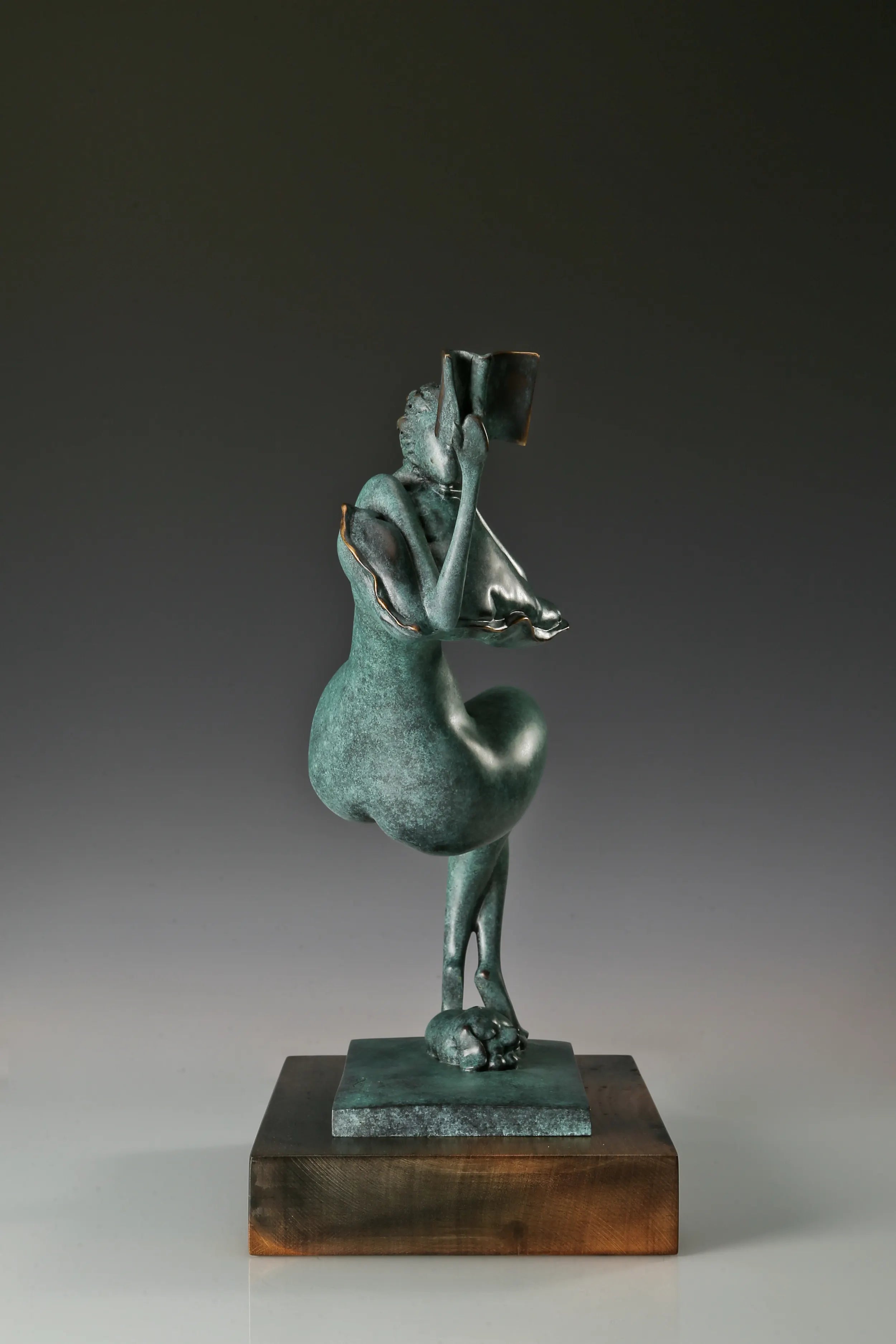 Narrow side view of the bronze female figure with bent legs, raised book, and wooden base