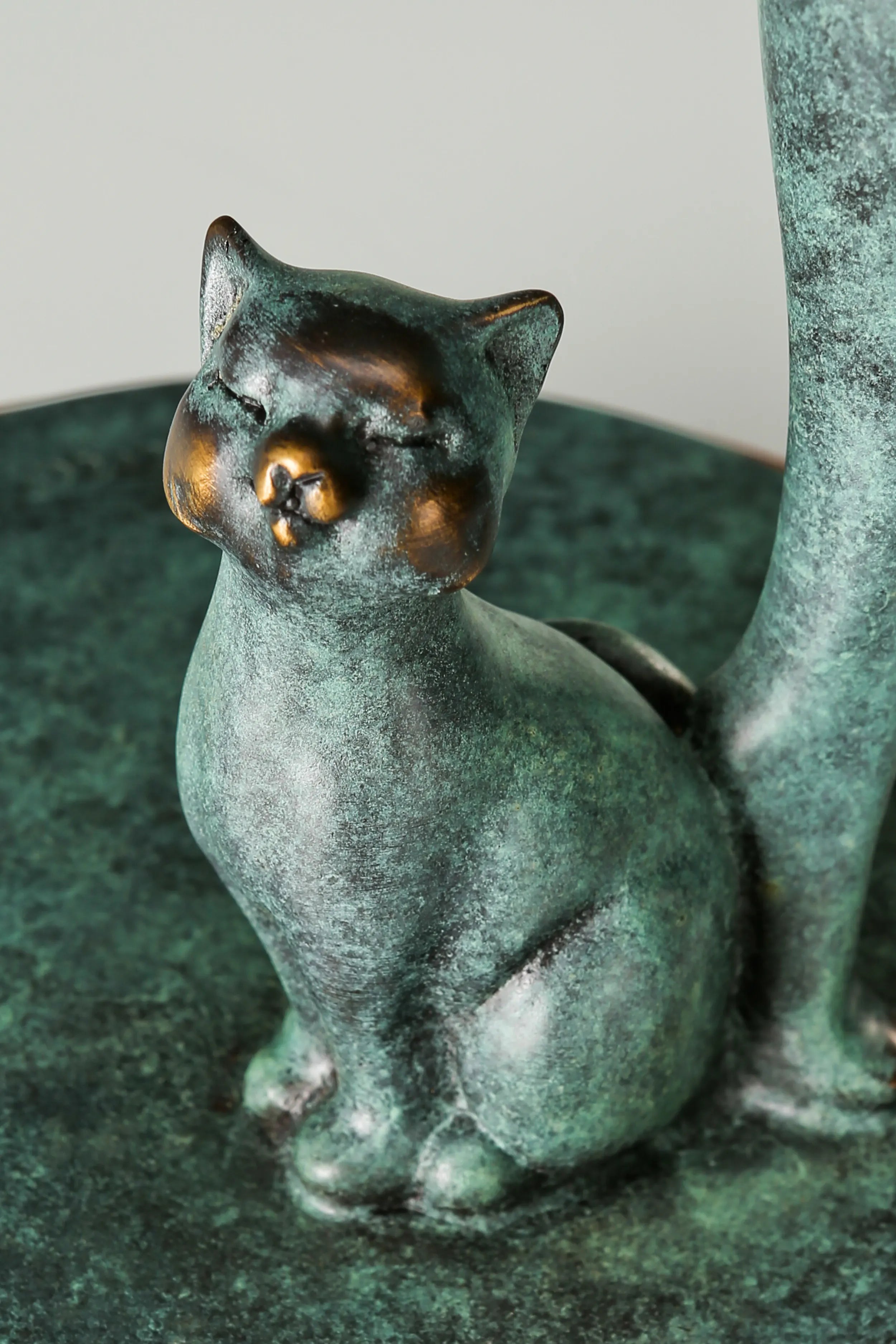 Close-up of a small bronze cat with golden facial accents sitting at the woman's feet