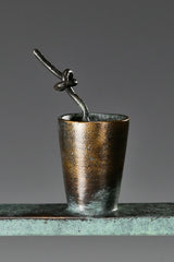 Close-up of a miniature bronze drink cup with a straw beside the seated woman