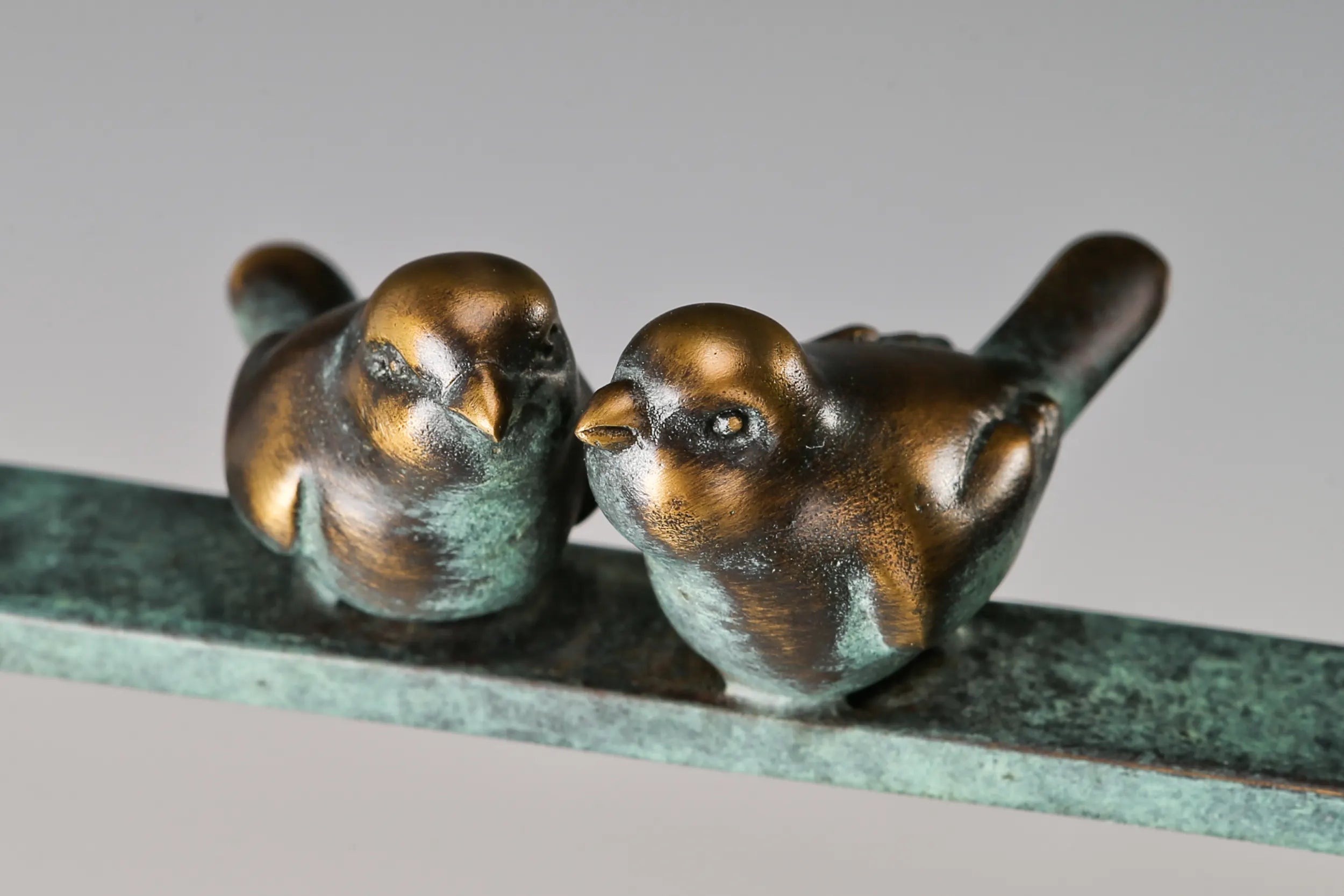 Close-up of two small bronze birds with golden accents perched on the sculpture's horizontal bar