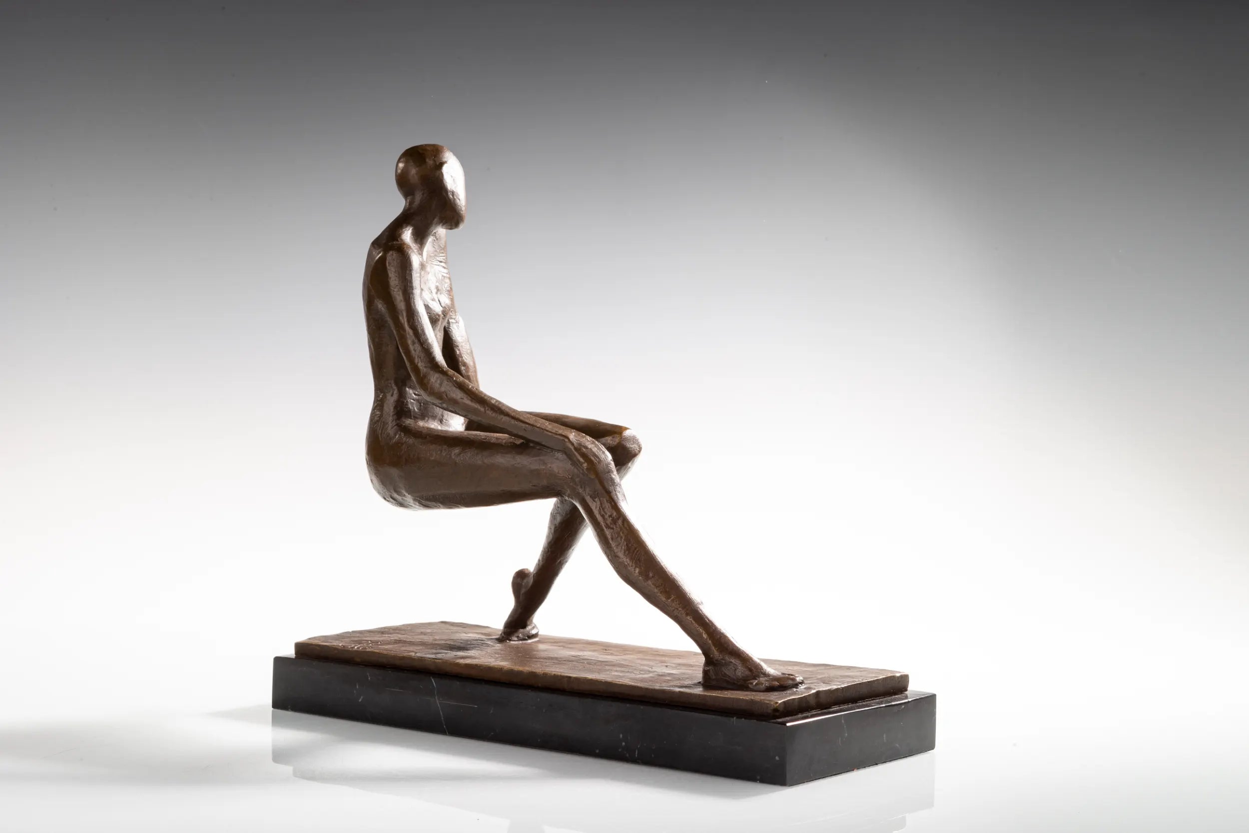 Side profile of seated bronze woman with relaxed posture and crossed legs