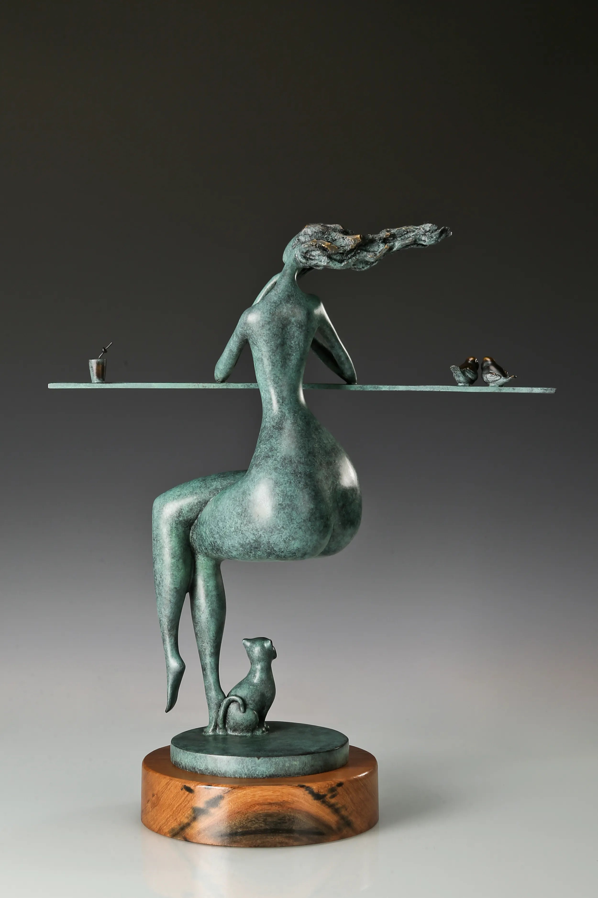 Rear view of an abstract woman sculpture with flowing hair and a small cat at the base