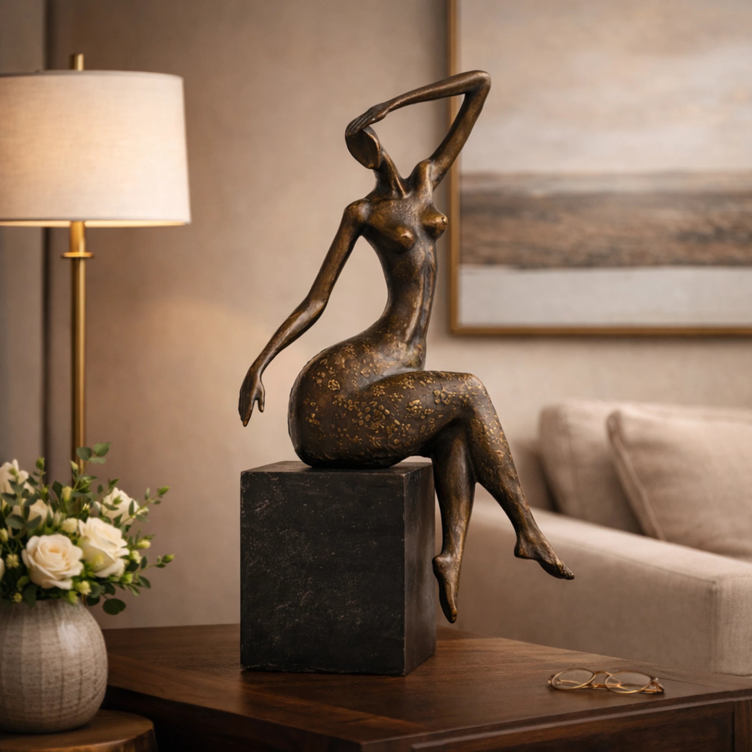 Contemporary abstract bronze seated female sculpture with golden floral motifs, graceful woman statue with raised arm on black marble base, loss wax casting modern art.