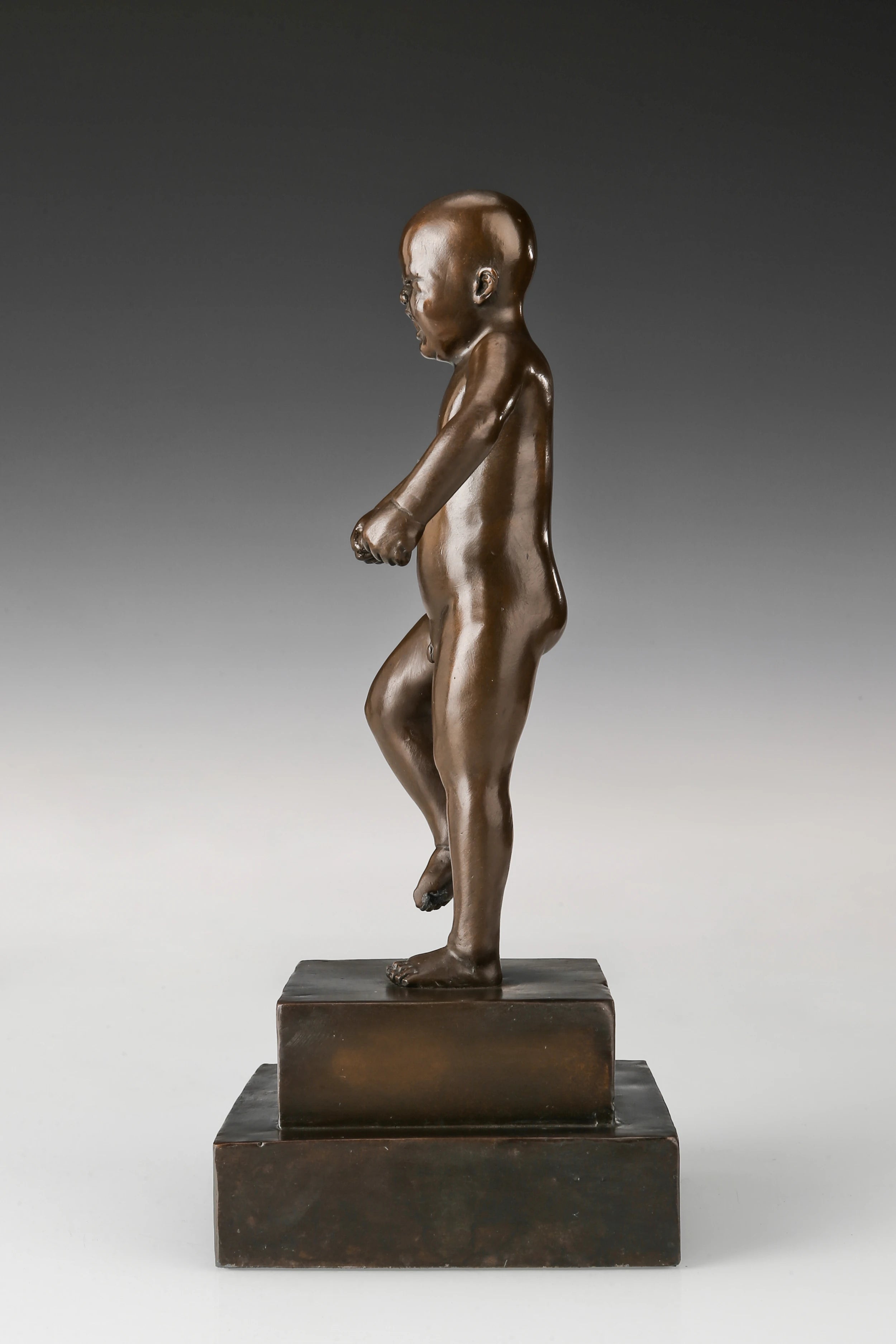 Left side view of bronze angry boy statue showing raised leg and clenched fist