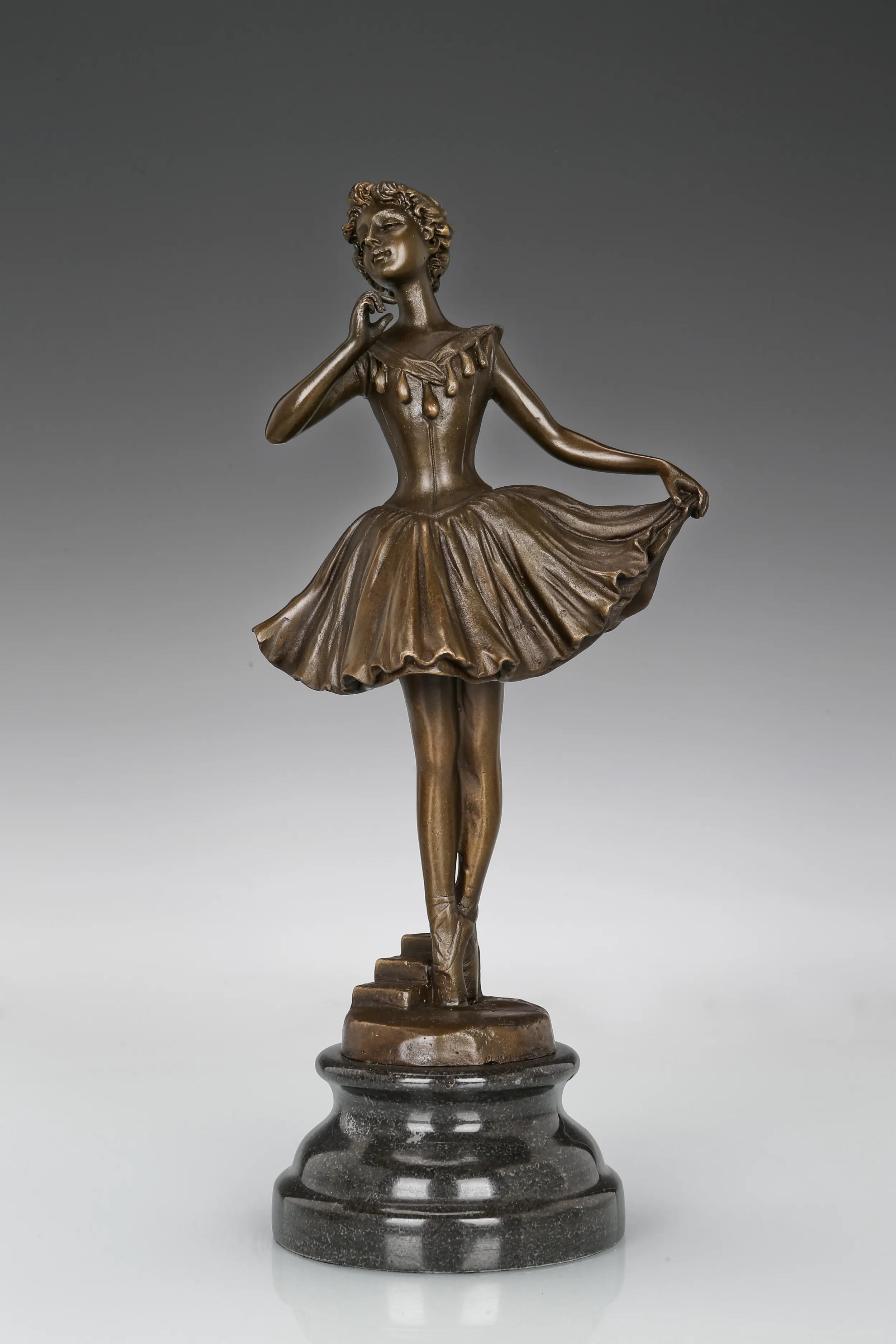 Front view of ballerina holding dress bronze sculpture with a flowing skirt