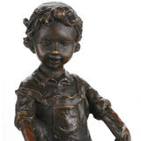 Close-up detail of bronze children sculpture showing facial expressions, clothing, and wheelbarrow texture.