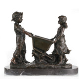 Nostalgic bronze sculpture of a boy and girl with a wheelbarrow on black marble base, heartwarming children playing art for home decor.
