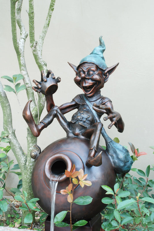 Whimsical bronze goblin garden fountain sitting on a large water jar with flowing water feature
