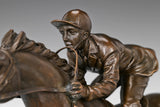 Close-up of bronze jockey figure showing forward riding position, racing clothing, and saddle details