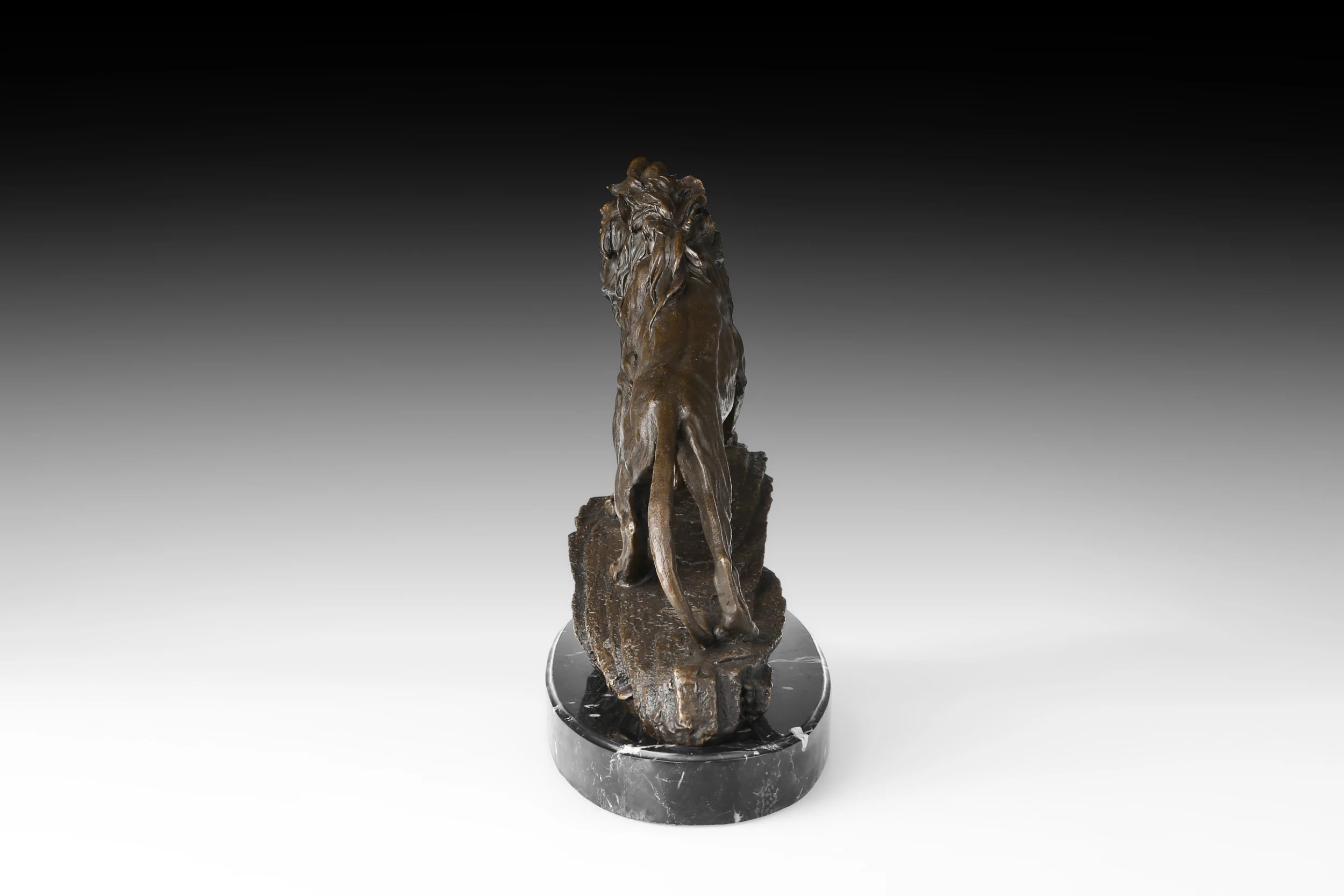 Rear view of bronze lion sculpture showing muscular hindquarters, tail, and textured rocky base