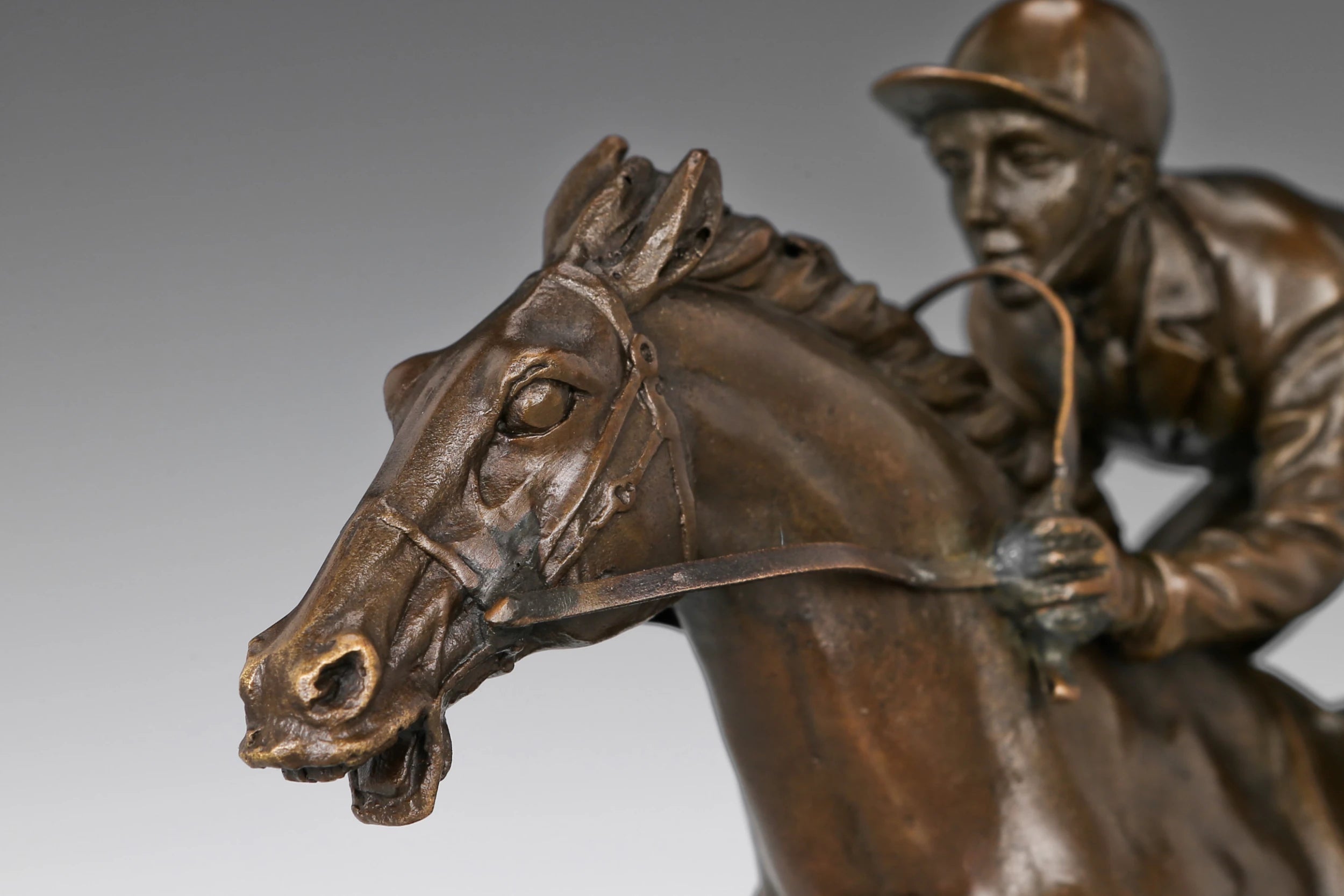 Close-up of bronze racehorse sculpture showing detailed head, bridle, reins, and racing expression