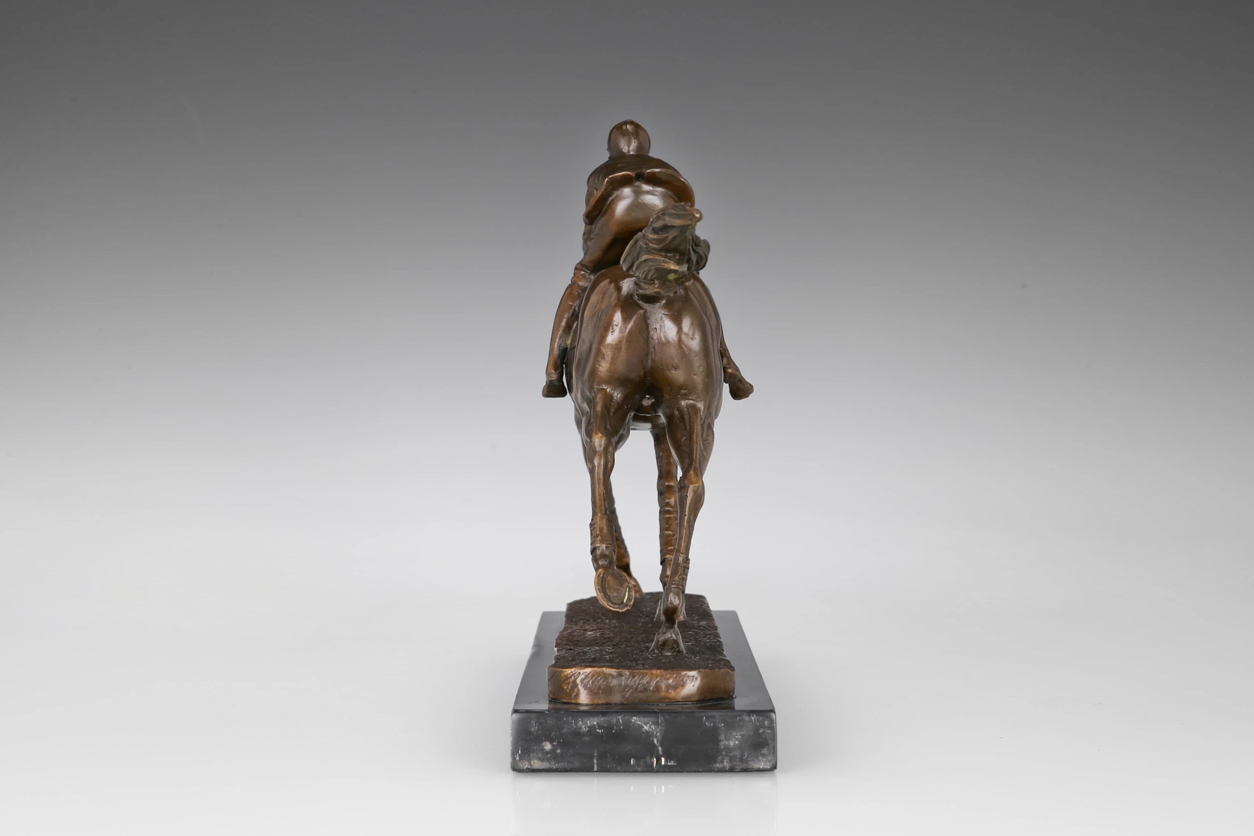 Rear view of bronze racehorse and jockey sculpture showing flowing tail and racing posture