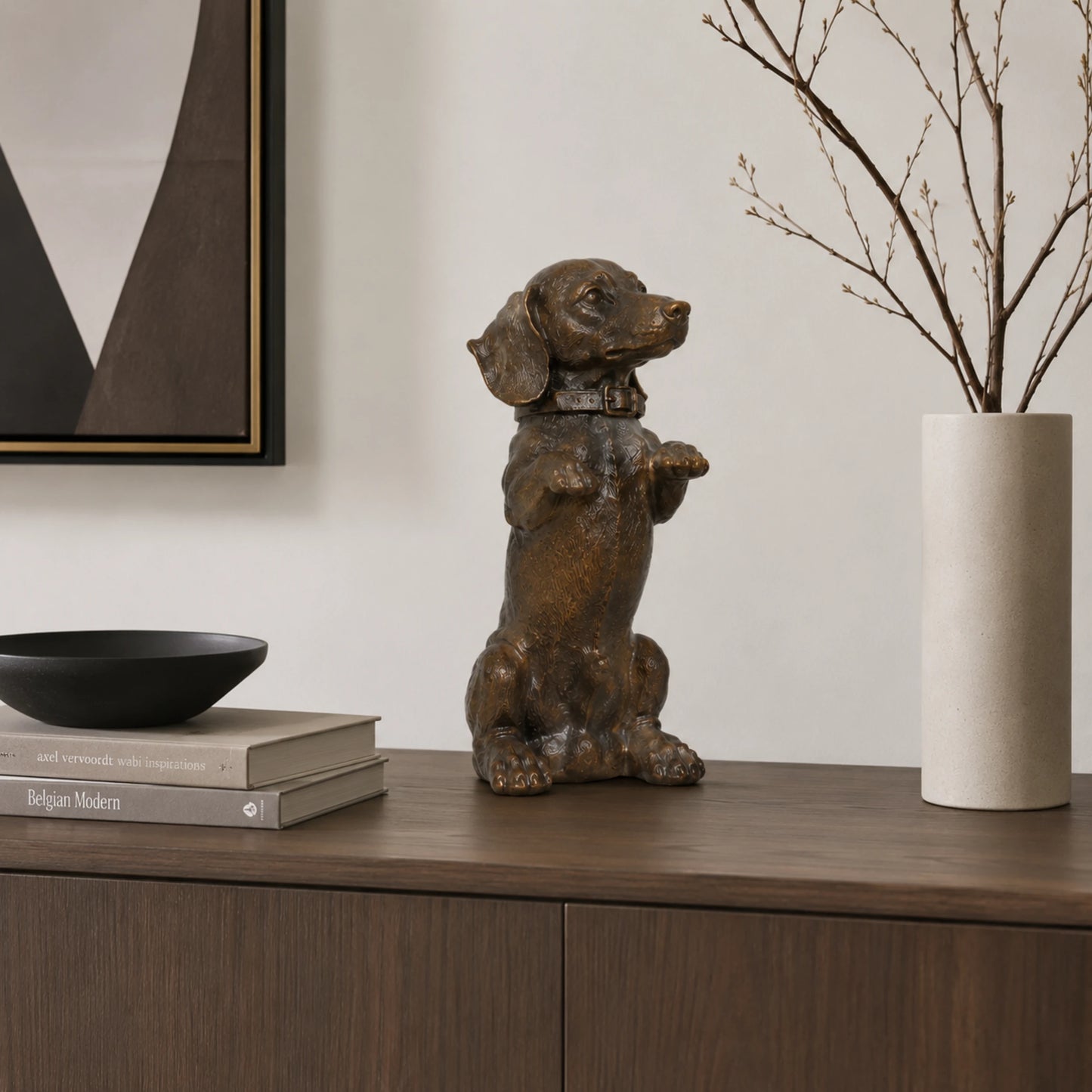 A charming bronze dachshund statue in a playful upright seated pose with front paws raised begging, highlighting its long body and short legs.