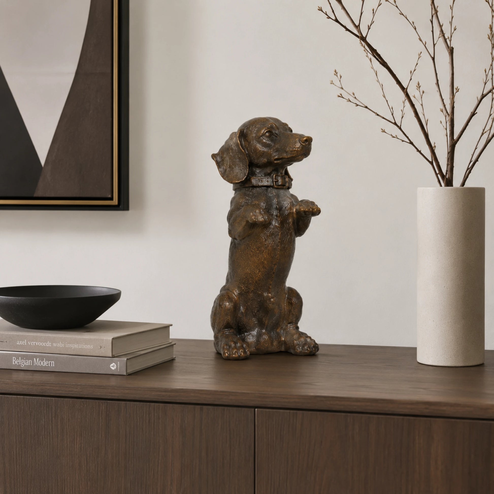 A charming bronze dachshund statue in a playful upright seated pose with front paws raised begging, highlighting its long body and short legs.