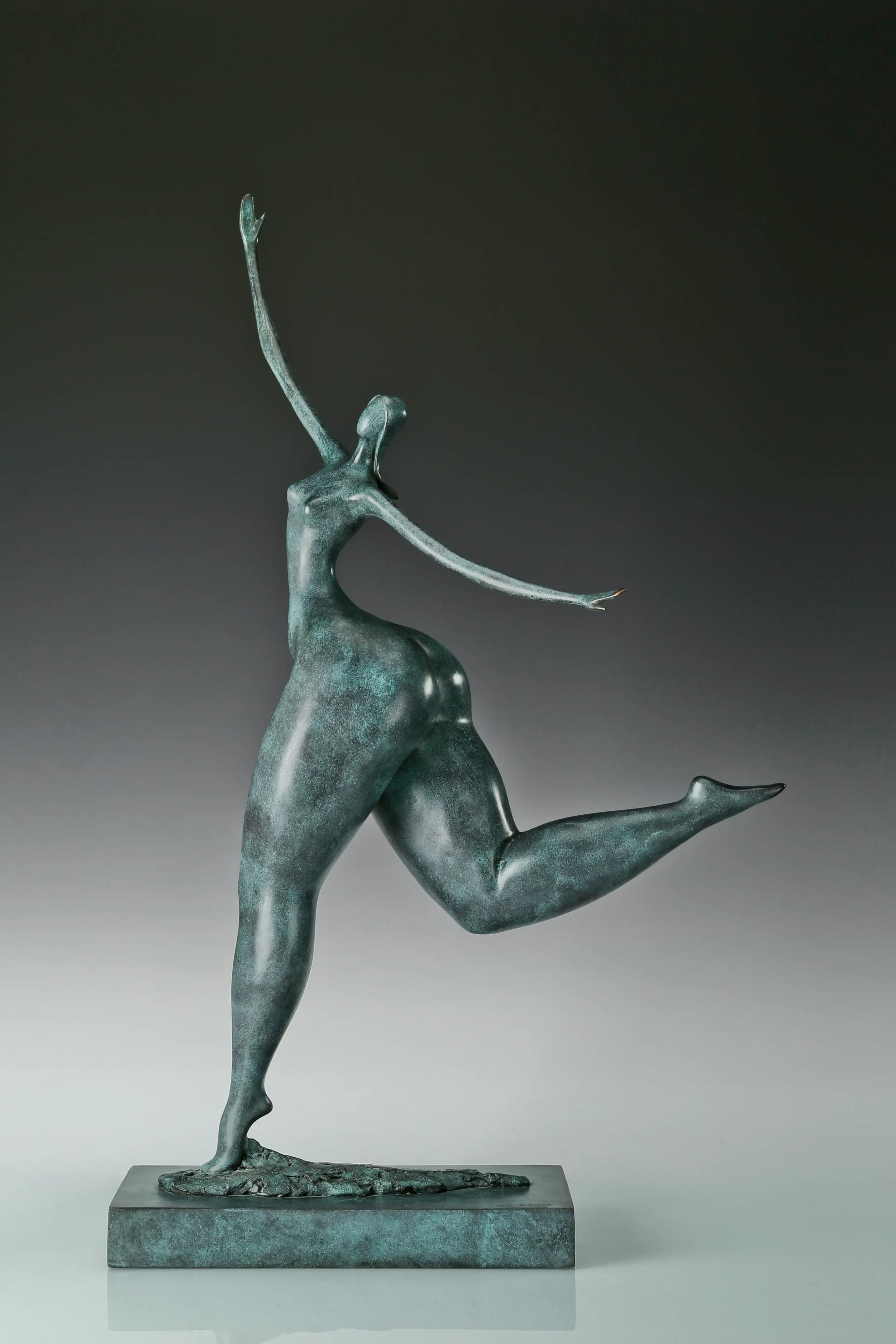 Left side view of green patina contemporary female dancer statue with a raised leg