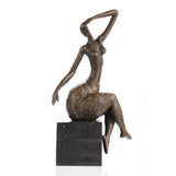 Contemporary abstract bronze seated female sculpture with golden floral motifs, graceful woman statue with raised arm on black marble base, loss wax casting modern art.