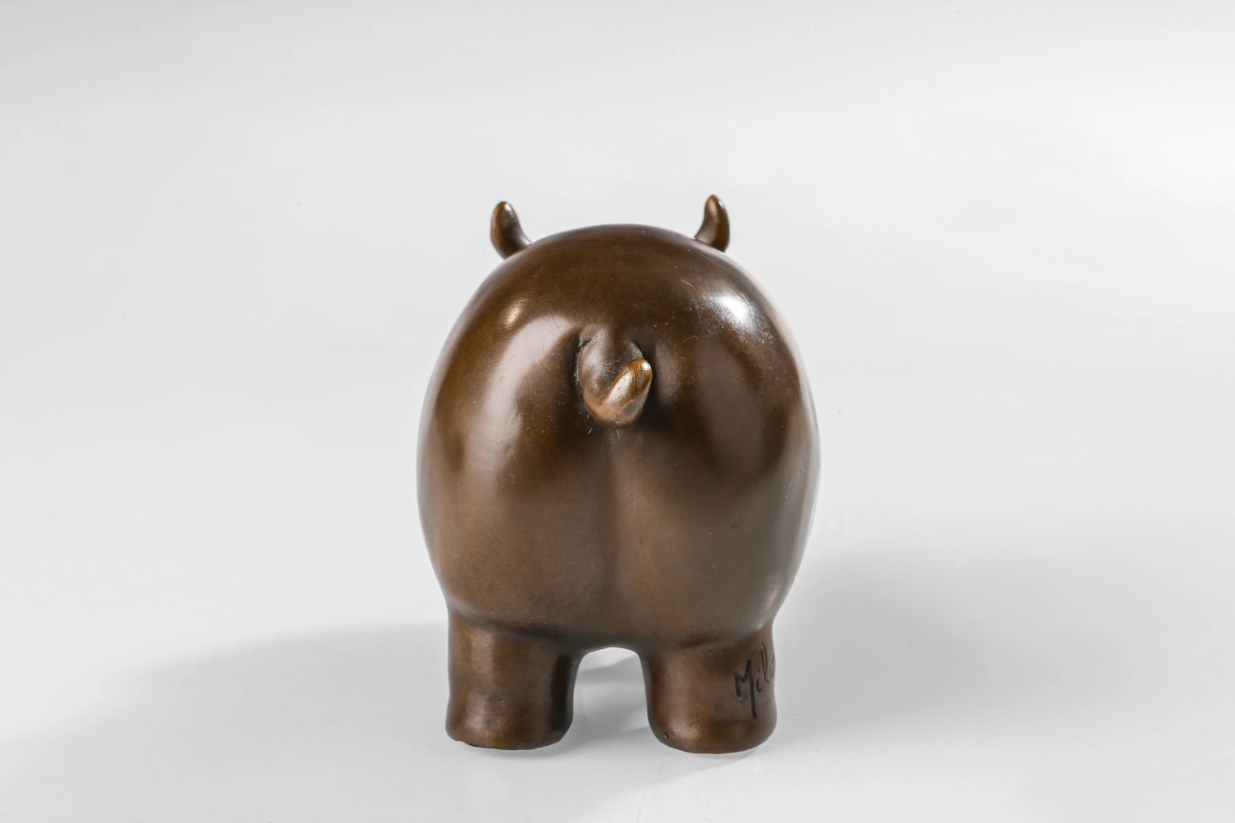 Rear view of a solid bronze cow statue featuring a minimalist rounded design.