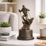 This is a dynamic bronze sculpture of a skier, crafted using the lost-wax casting method. The piece captures the athlete mid-action, navigating a rugged, snow-like terrain with ski poles firmly in hand and legs bent in a powerful stance. The rich, warm bronze patina accentuates the fluid folds of the skier’s jacket and pants, as well as the textured, naturalistic base that simulates a snow-covered slope.