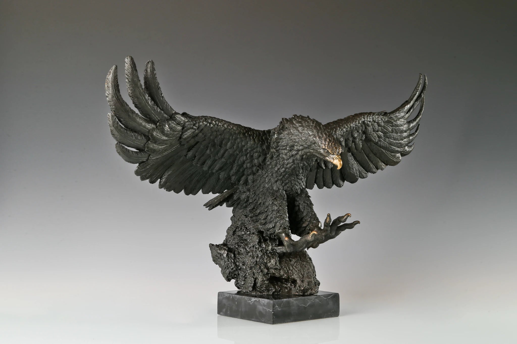 a majestic bronze sculpture of a bald eagle, crafted using the lost-wax casting method. The piece captures the raptor in a dynamic, predatory pose—wings fully spread, talons extended forward, and head tilted downward with a piercing gaze—conveying raw power, precision, and the primal intensity of a hunting strike.