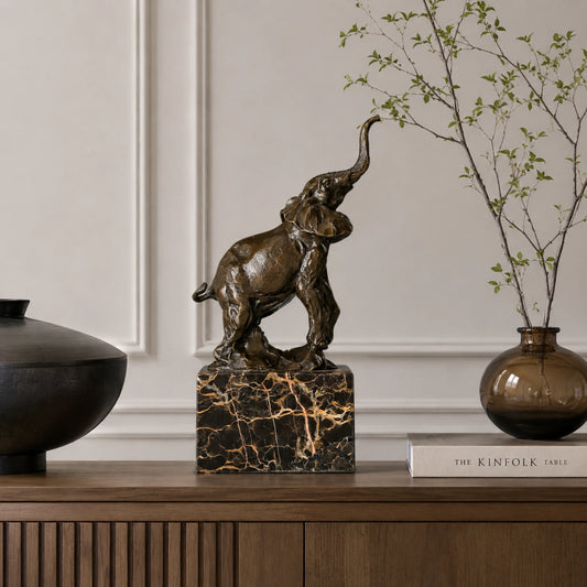 A lifelike bronze elephant sculpture with its trunk raised high on a black marble plinth, a symbol of good fortune and strength for home decor.